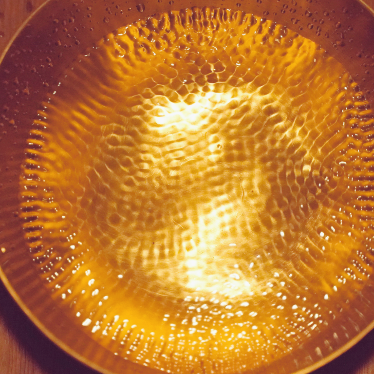 Klangschale mit Wasser gefüllt, mit gewelltem, strukturiertem Muster.